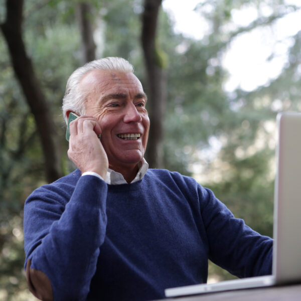 older financial professional talking on cell phone while reviewing client information on laptop