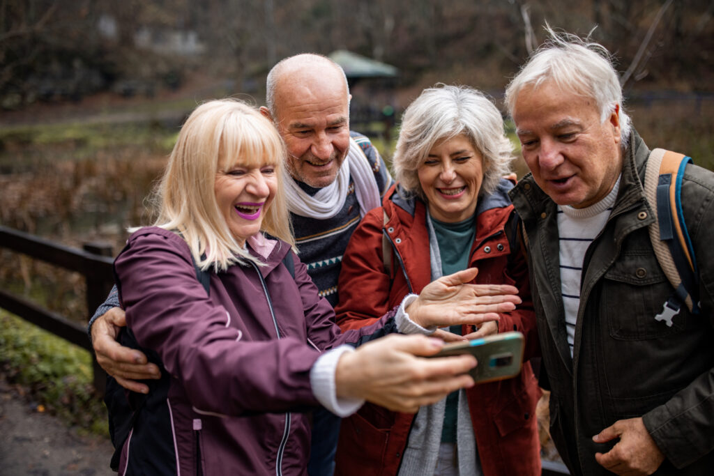 Group of people, two mature couples taking a selfie together with smart phone in nature on a cloudy autumn day together.