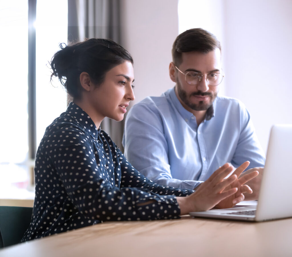 young man with glasses sitting at laptop with woman coworker in office setting