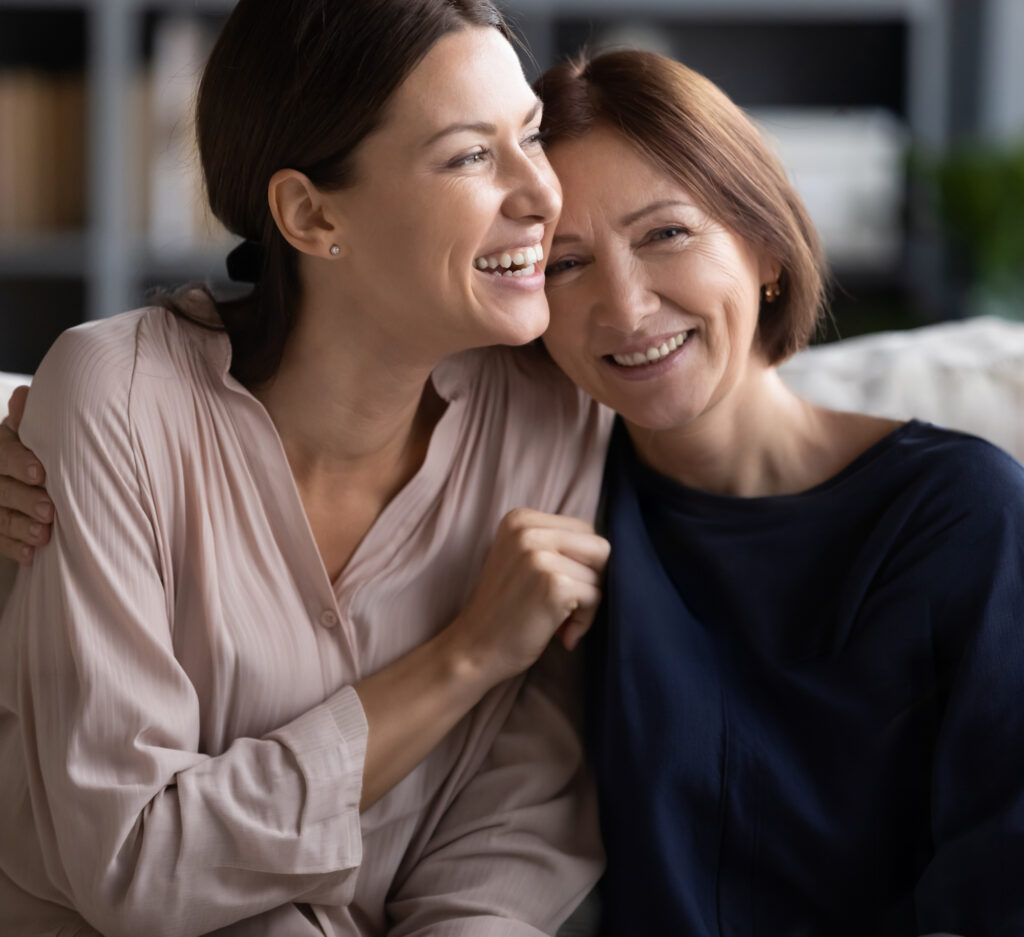 Two women embracing with a smile. one older than the other.