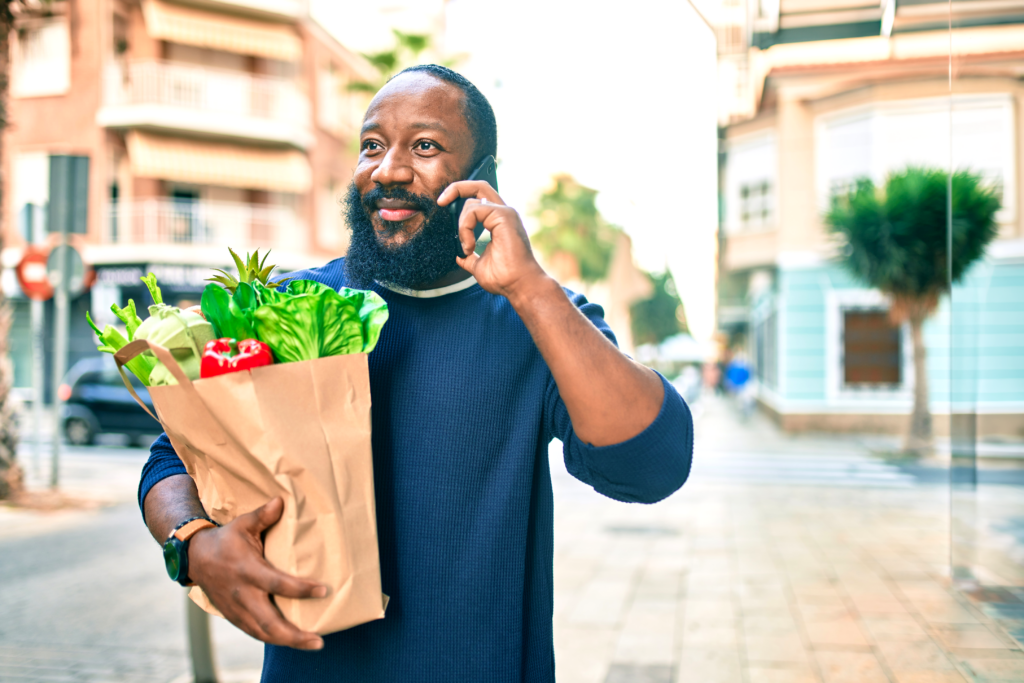 Man walking in the street while talking on his cell phone and carrying a grocery bag of fresh vegetables